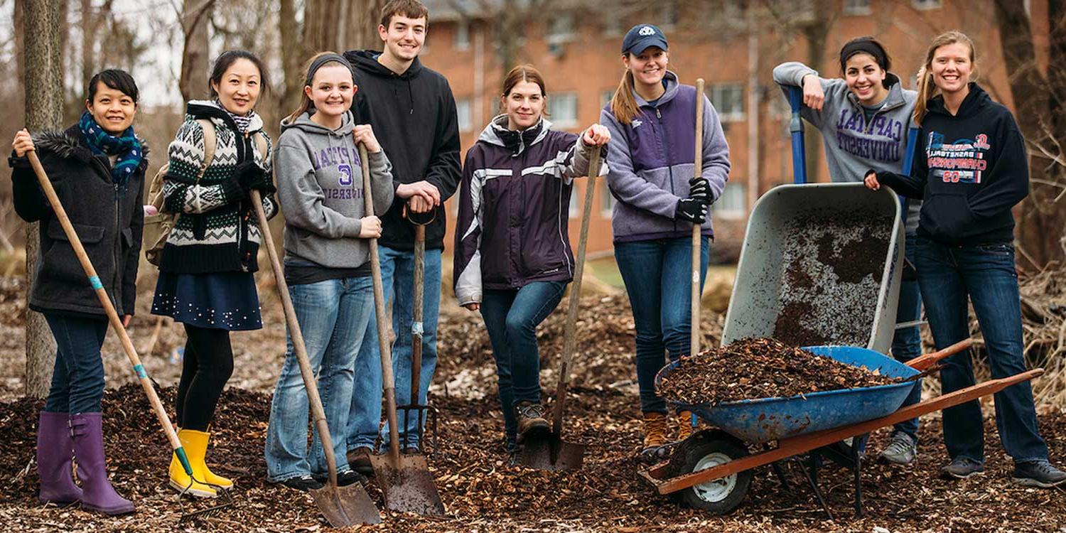 student community service team outside in mulch holding shovels and wheel barrows