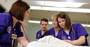 nursing students in capital uniforms standing around a patient bed